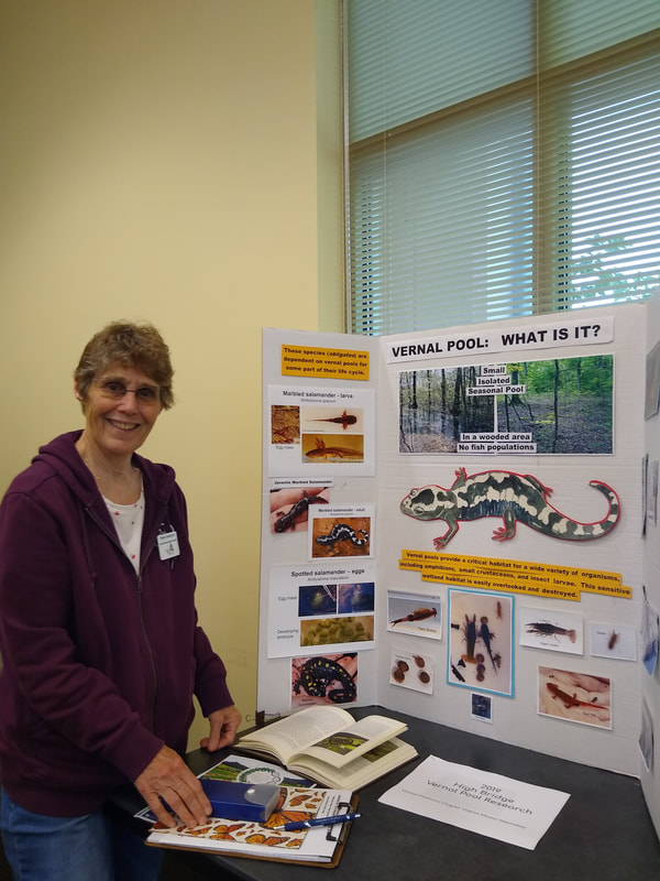 A smiling woman stands beside a display about vernal pools