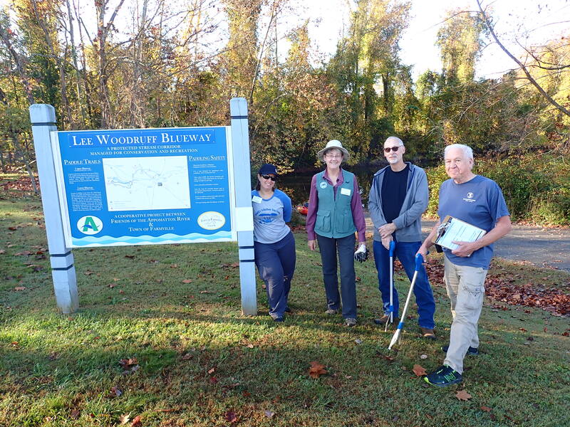 Four people stand beside the Lee Woodruff Blueway sign on an autumn day