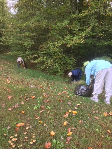 Three people put grass into black garbage bags on a fall day